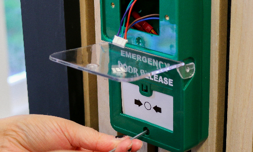 Emergency break glass unit with the cover lifted and cover being removed using an allen key