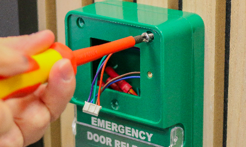 A screwdriver taking the cover off of an emergency break glass unit