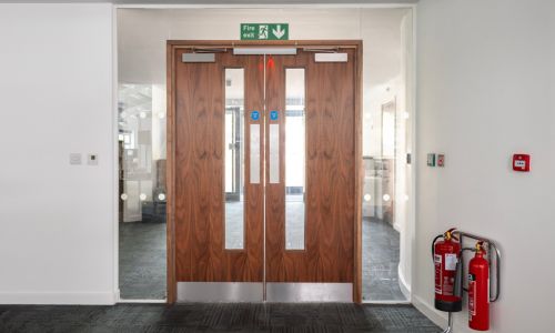 A pair of fire rated doors. They have door closers, a double maglock, and fire signage installed, with fire extinguishers to the side.