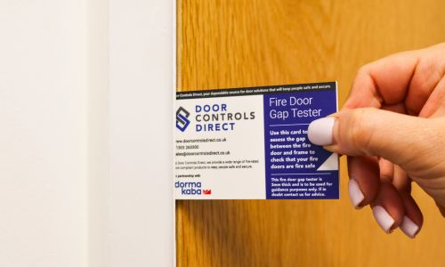 Door Control Direct and dormakaba dual branded fire door gap tester held in a hand.